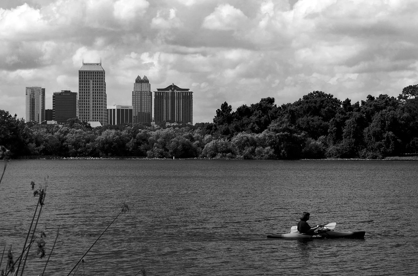 A kayaker on Lake Ivanhoe, seen from Ivanhoe Park in College Park, with the downtown Orlando skyline behind