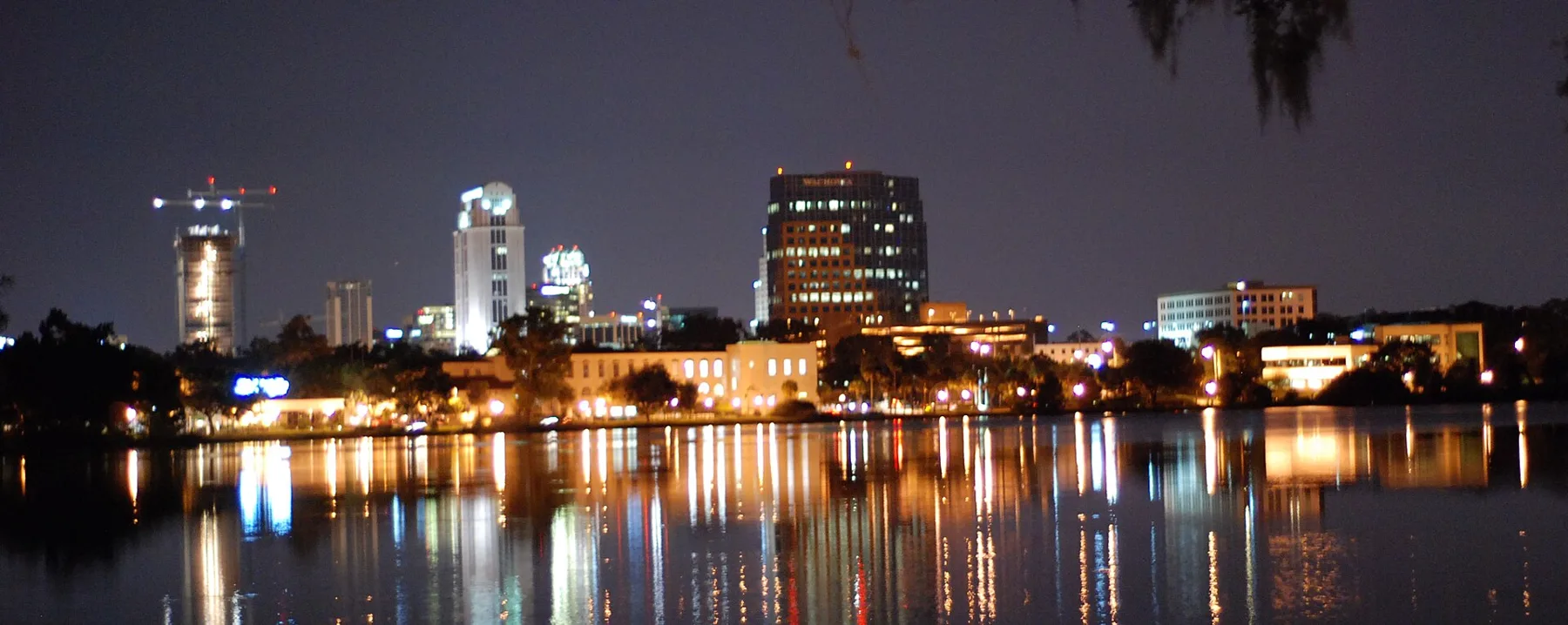 The downtown Orlando skyline at night, its lights reflected in a lake